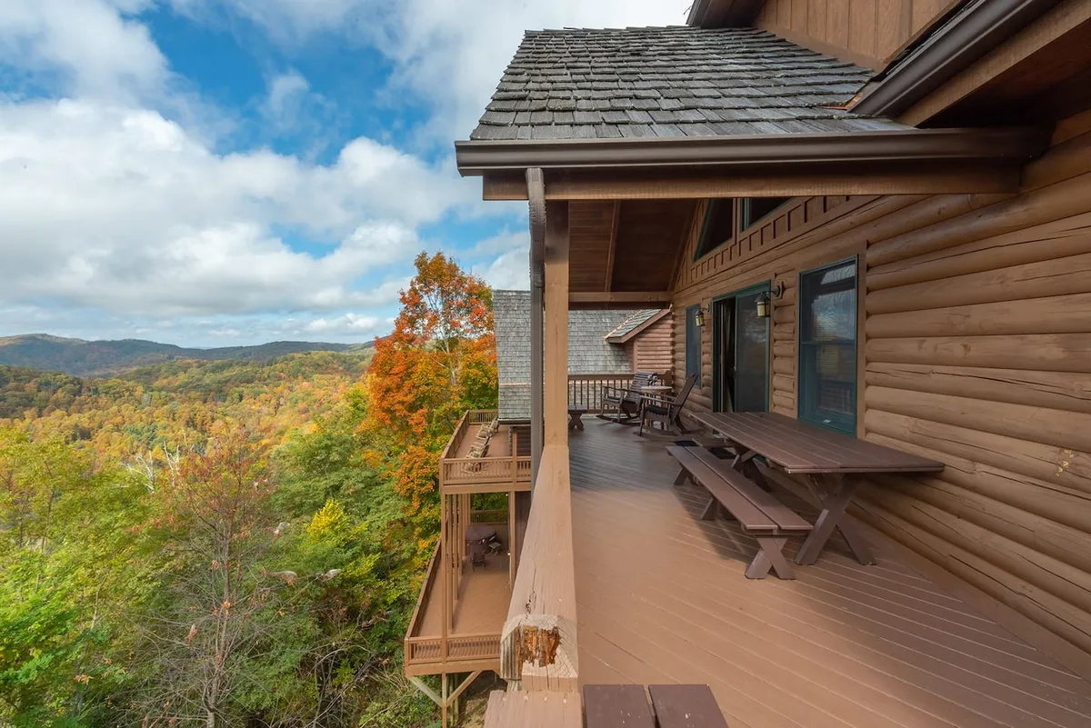 A wide wooden deck with ample seating overlooks breathtaking mountain views and vibrant autumn foliage. The deck is large enough for outdoor dining or group gatherings, extending the celebration space into the outdoors.