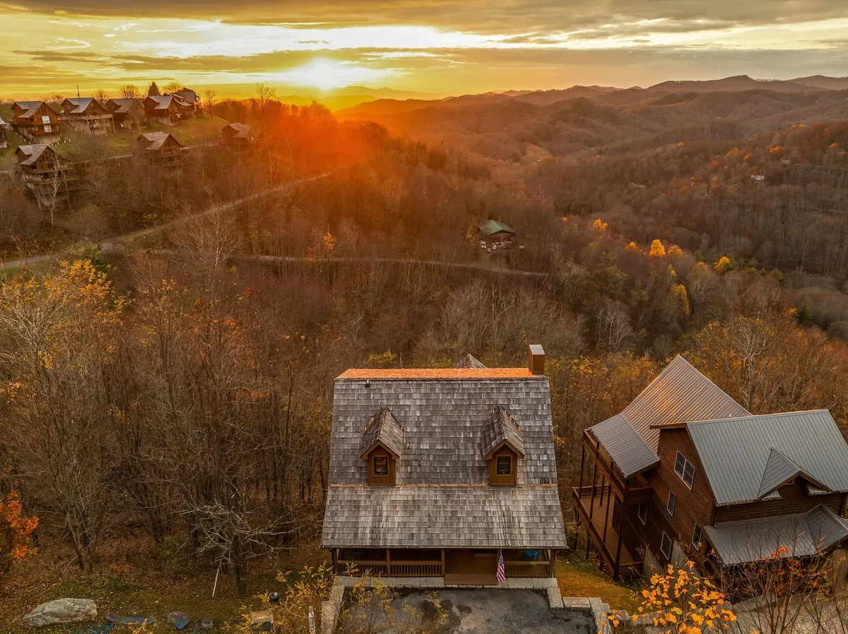 This image captures a stunning sunset over the Blue Ridge Mountains, with two rustic cabins nestled amid vibrant fall foliage. The warm glow of the evening light highlights the natural beauty of the landscape, evoking a sense of adventure and tranquility.