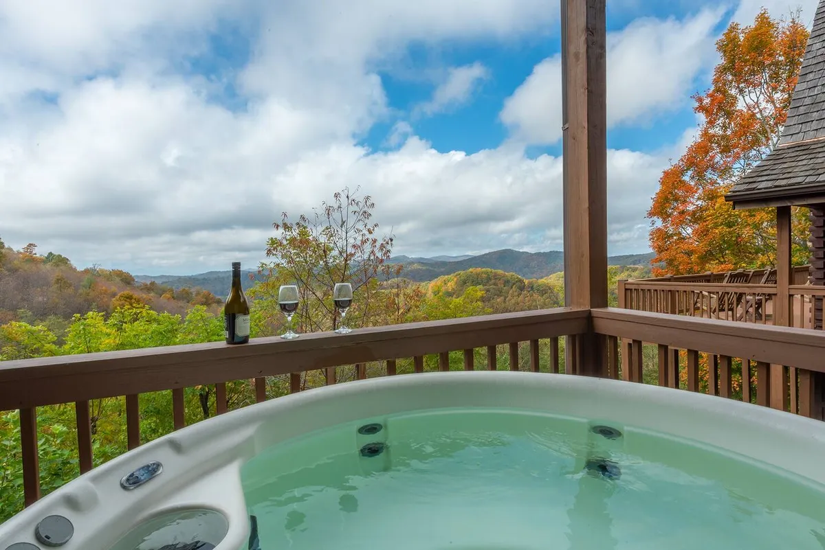 A hot tub with a wine bottle and glasses sits on a deck overlooking sweeping mountain views at sunset. The scene radiates tranquility and is perfect for an intimate evening under the stars.