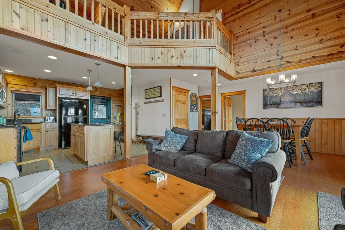 An open-concept living and dining space featuring a plush sofa, long wooden dining table, and an adjoining kitchen. Exposed beams and wooden floors add rustic charm, while the layout makes it easy to flow from one area to another—perfect for hosting groups or family get-togethers.